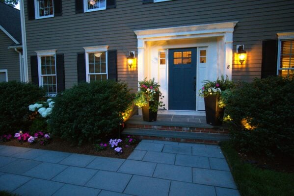 Professionally designed backyard landscape with stone patio, layered plantings, and New England architecture in Massachusetts