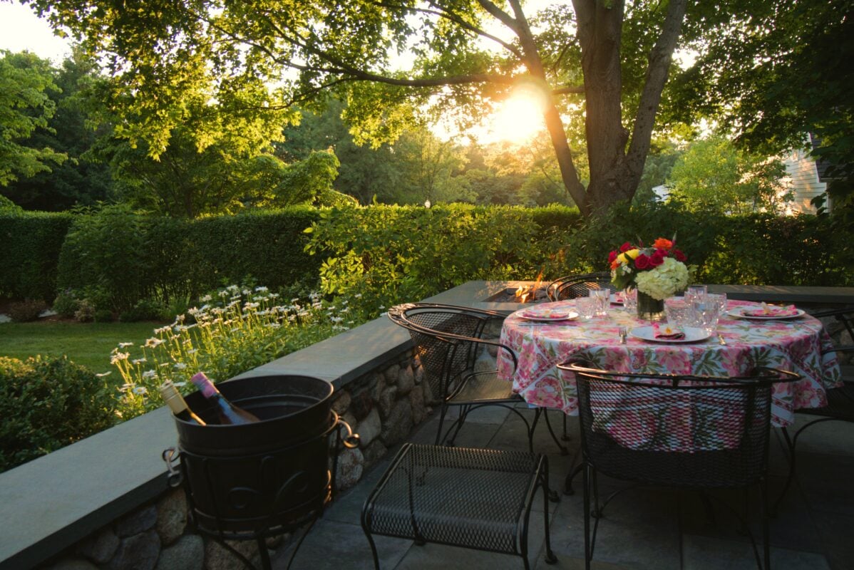 Stone patio with outdoor kitchen and pergola in a Massachusetts backyard at dusk