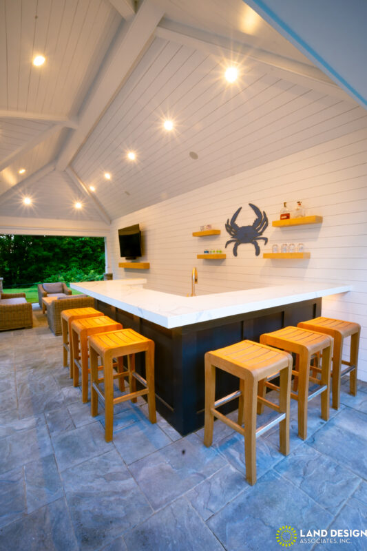 Covered outdoor kitchen with white marble countertop, dark cabinetry, and bar seating for eight, Massachusetts