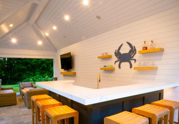 Covered outdoor kitchen with white marble countertop, dark cabinetry, and bar seating for eight, Massachusetts